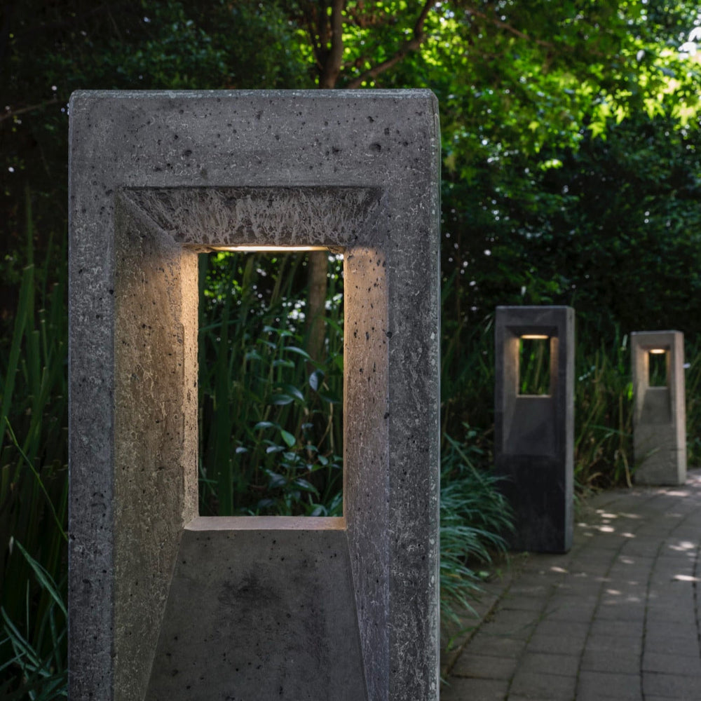 Concrete outdoor lamp post with a rectangular cutout in a garden setting.