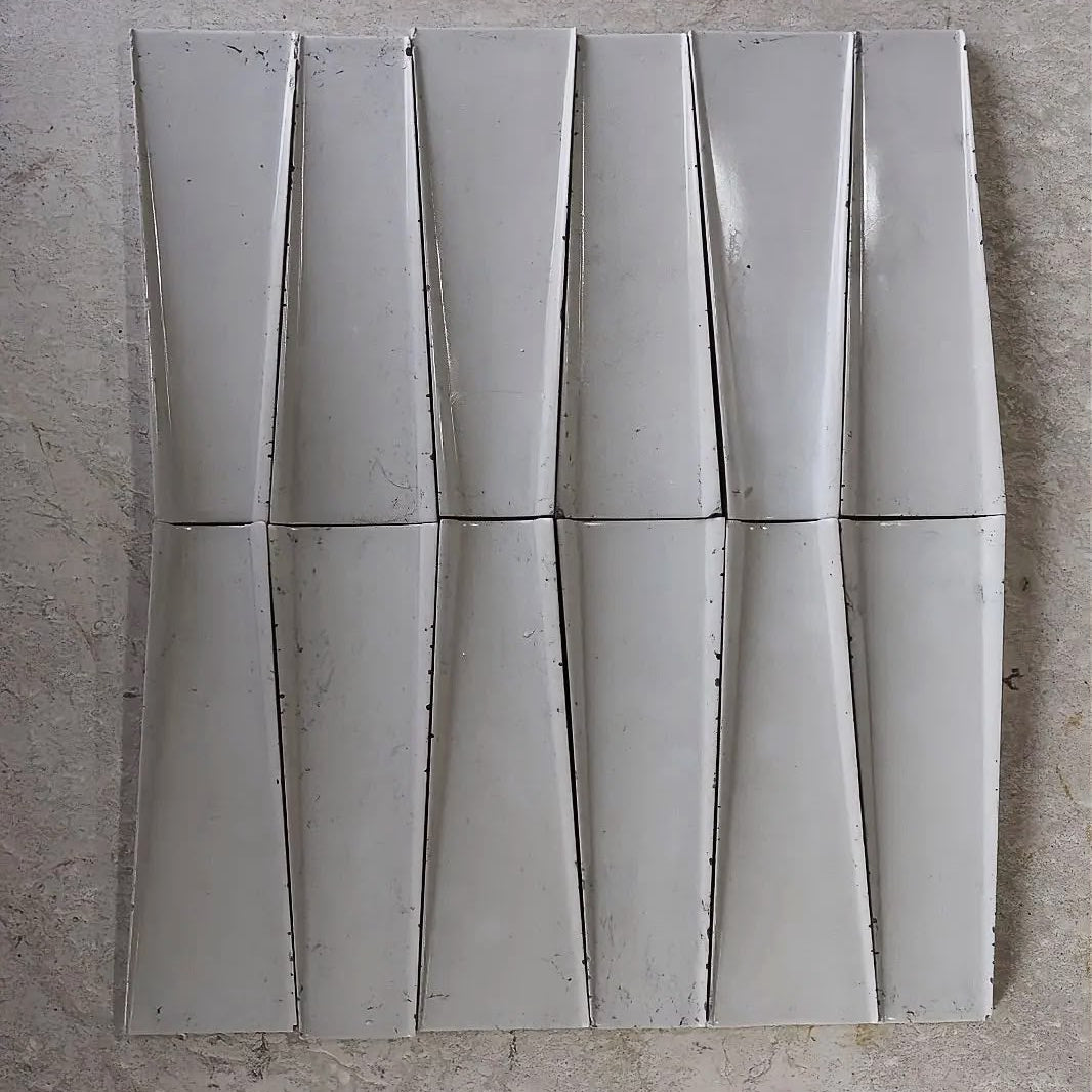 
                  
                    A set of light gray rectangular wall tiles arranged in a grid on a textured beige stone surface.
                  
                