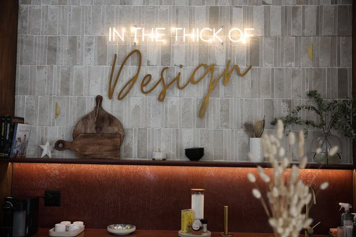Neon sign reading 'In the Thick of Design' on a tiled wall with decorative elements.